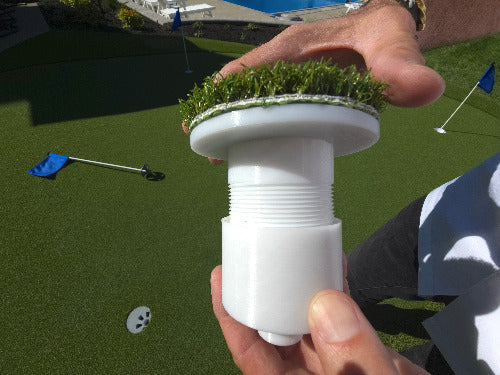 White adjustable golf cup insert being held by hands on top and bottom over top a putting green
