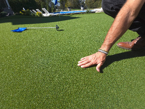 Man with hand on top of golf cup insert inside of golf cup on putting green with blue golf flag in back ground
